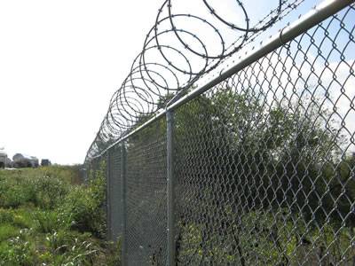 Razor wires are installed at the top of chain link fencing in he farmland.